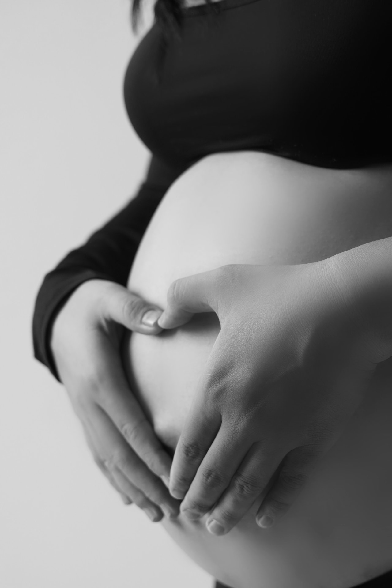 A pregnant woman sitting on the edge of a bed in soft morning light